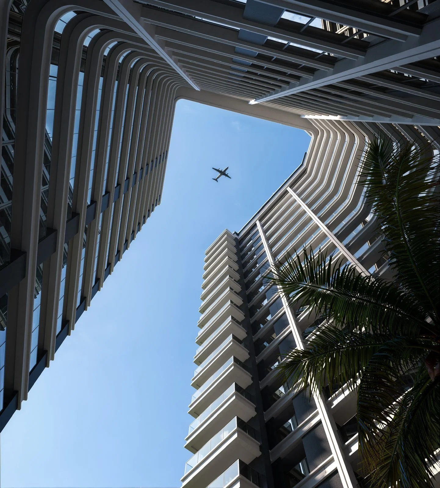 Upward view of Balkis Residences, Riverside Drive, with curved balconies, palm fronds and an aeroplane overhead.