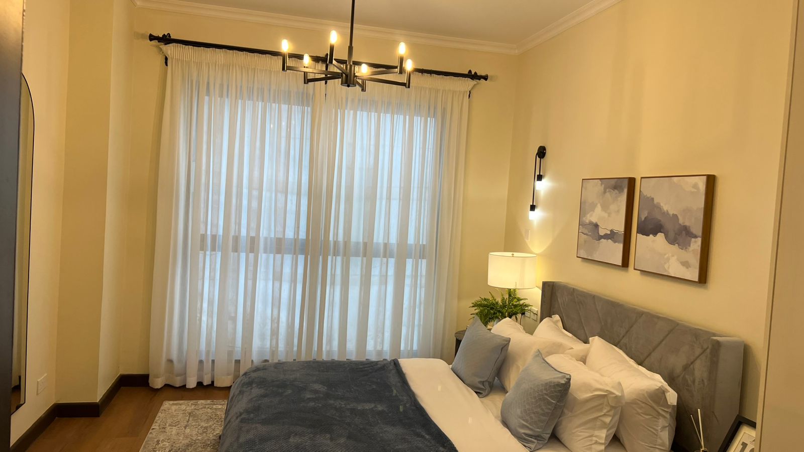 Bedroom at Beacon by Synina, Kileleshwa, with a grey upholstered headboard, sheer curtains and framed abstract art.