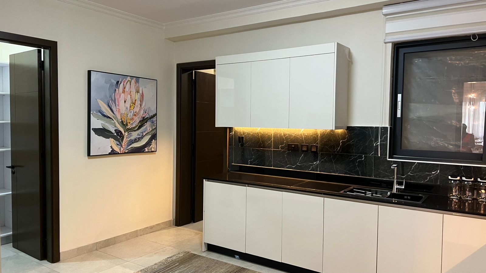 Kitchen at Beacon by Synina, Kileleshwa, with white cabinets, black veined backsplash and a sink beneath the window.