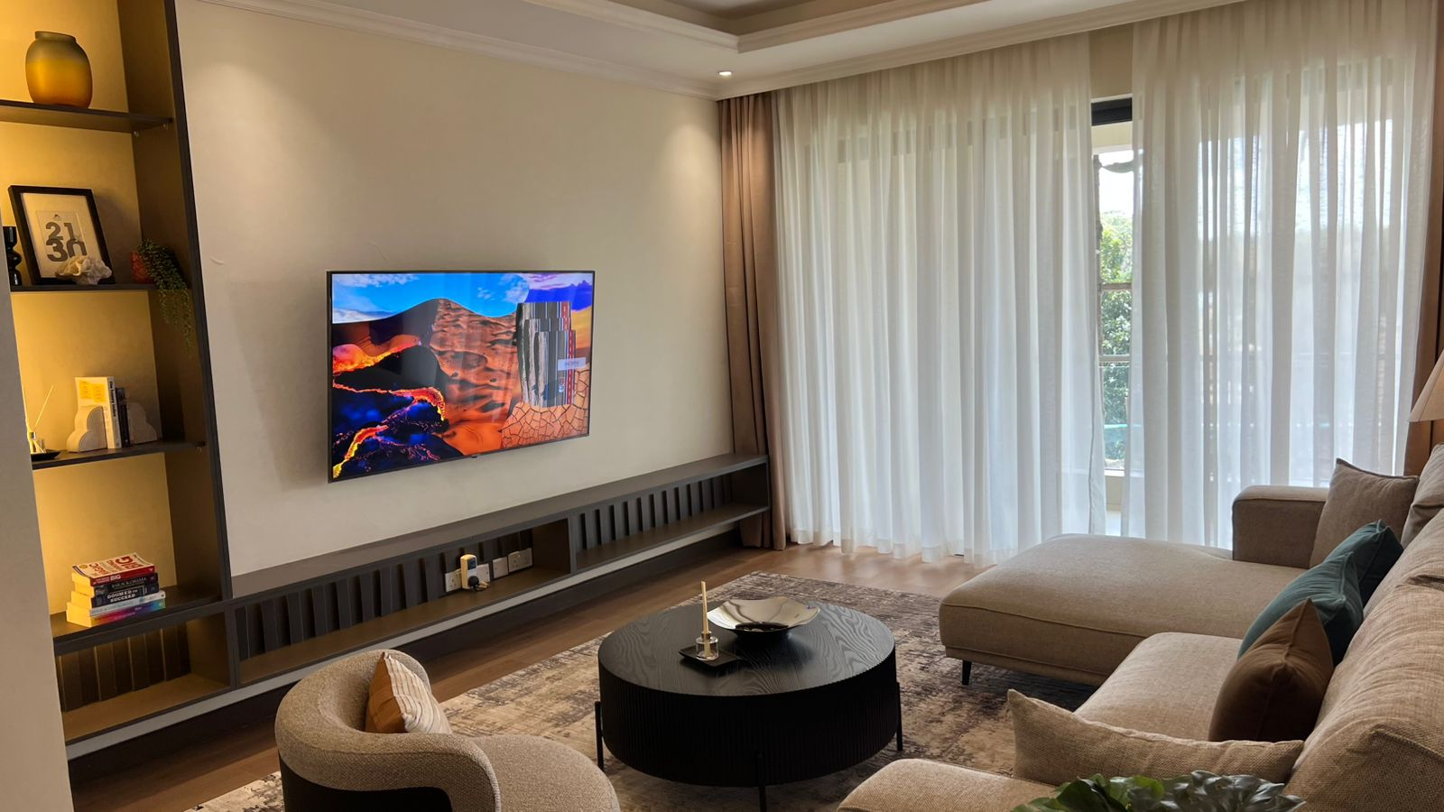Living room at Beacon by Synina, Kileleshwa, with beige sectional sofa, round coffee table and sheer curtains.