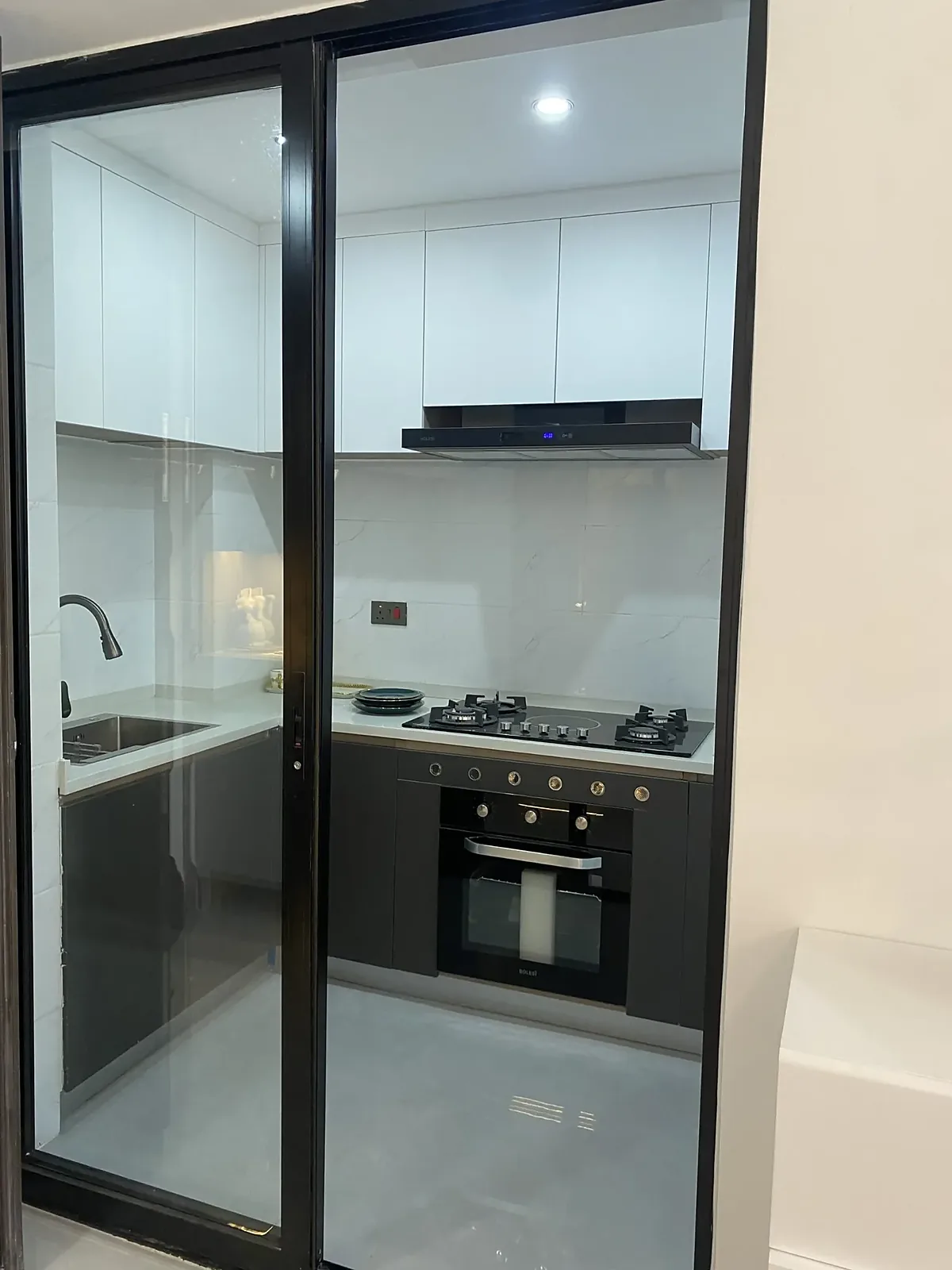 Kitchen at Capital Garden, Hurlingham, with black-framed glass doors, white cabinets, a gas hob and built-in oven.