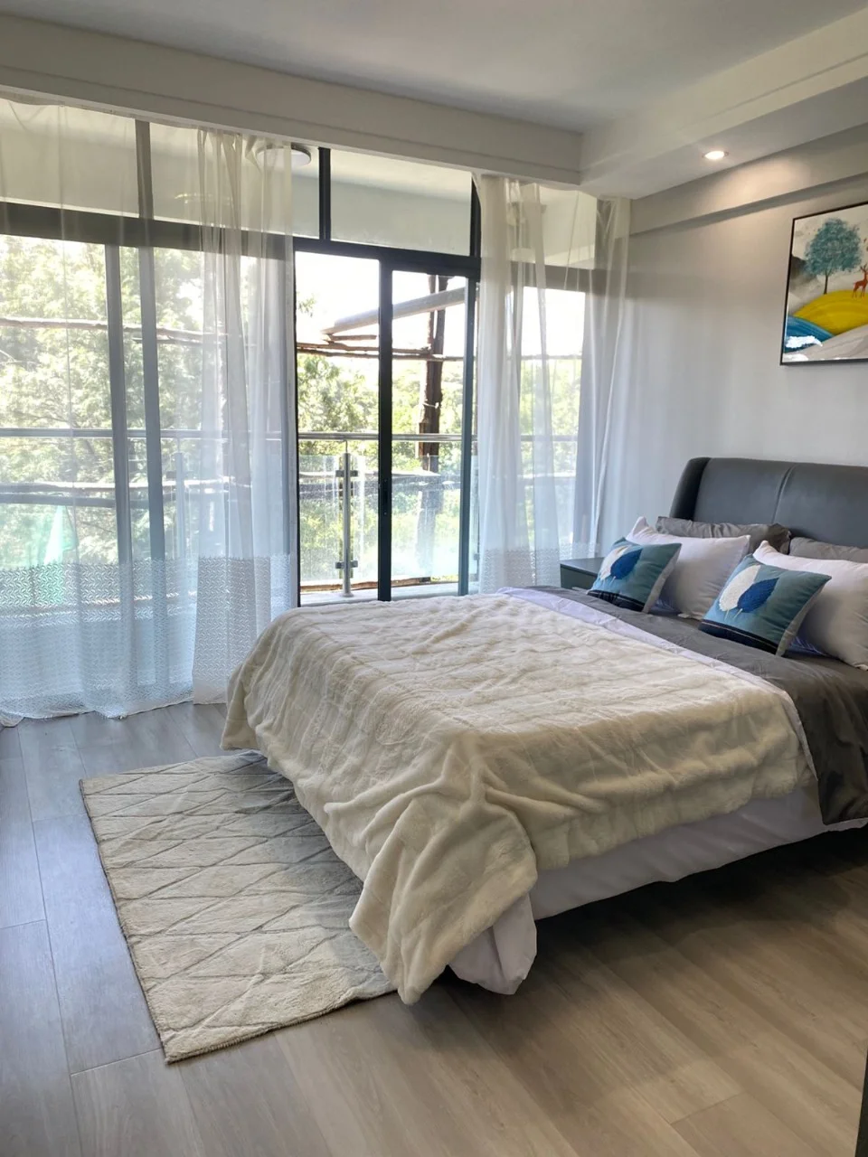 Bedroom at Golden Street Residency, Kileleshwa, with an upholstered headboard, sheer curtains and glass balcony doors.