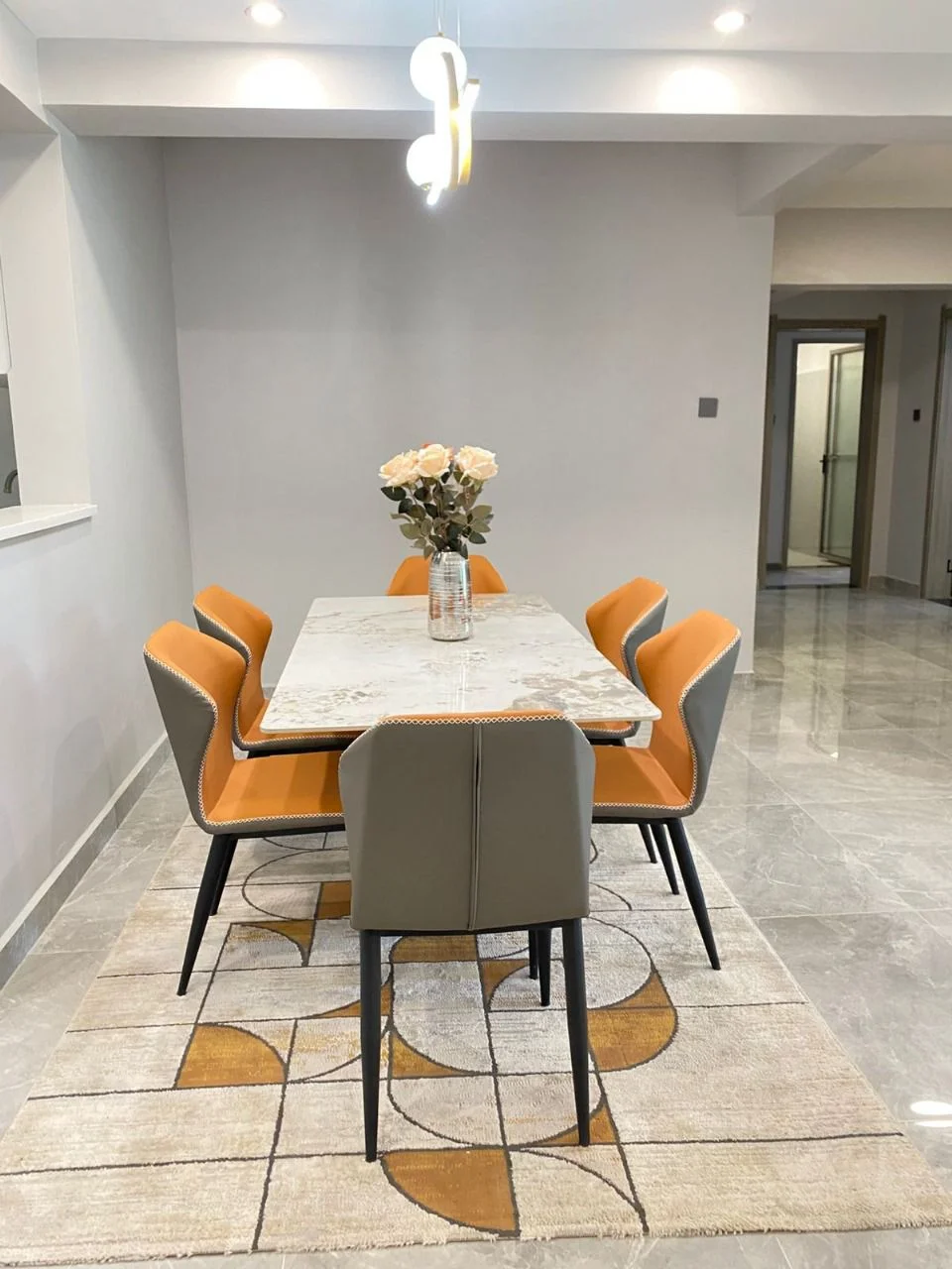 Dining table with orange and grey chairs on a patterned rug at Golden Street Residency, Kileleshwa.