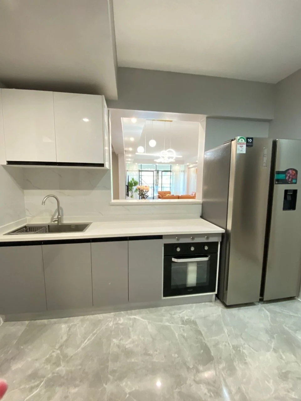 Kitchen at Golden Street Residency, Kileleshwa, with white and grey cabinets, sink, built-in oven and side-by-side refrigerator.