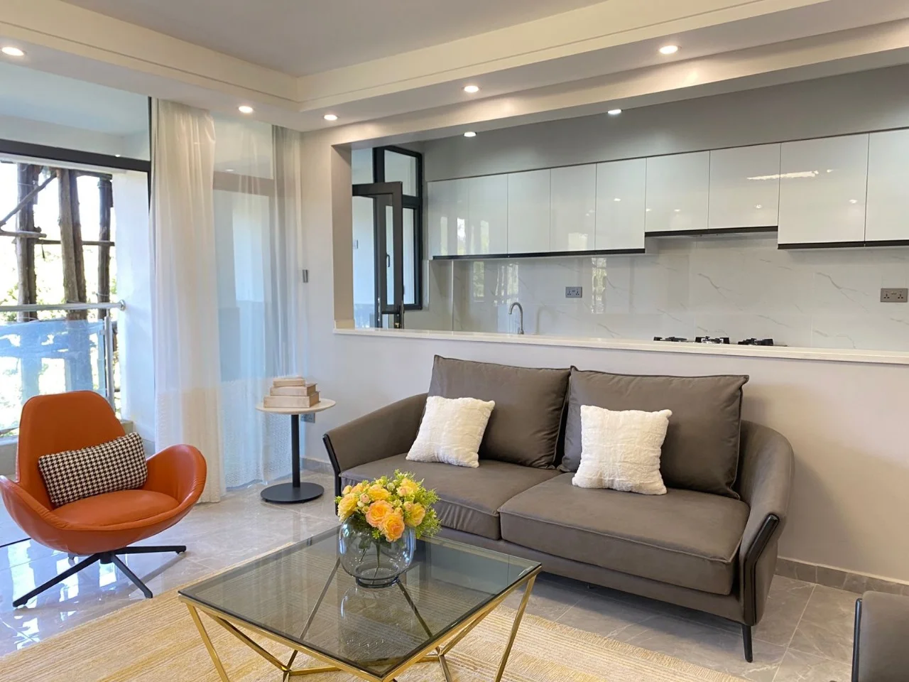 Living area at Golden Street Residency, Kileleshwa, with grey sofa, orange chair and kitchen beyond.