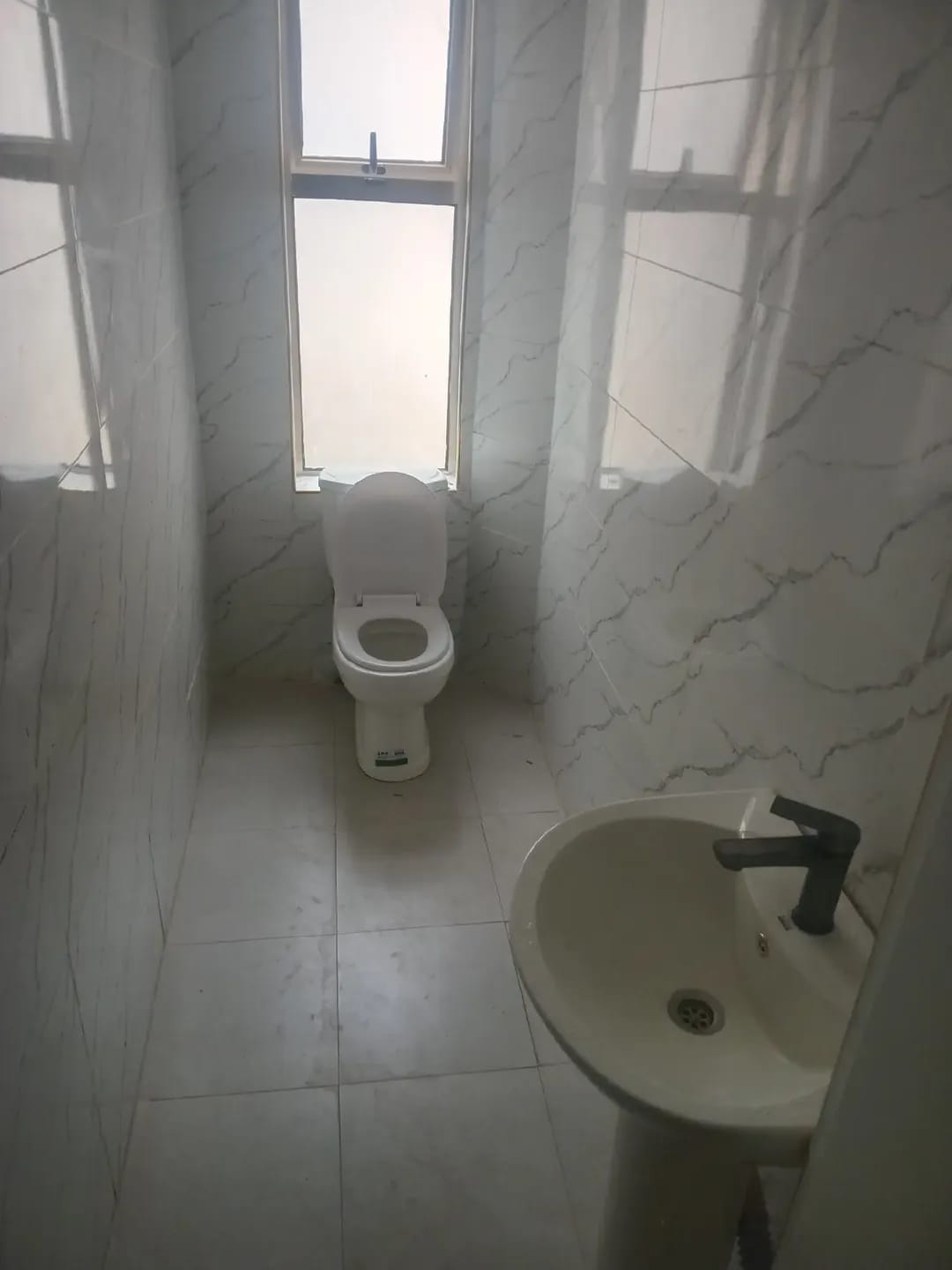 Karen, Kerarapon bathroom with a toilet, pedestal basin, black tap, marble-effect wall tiles and a frosted window.