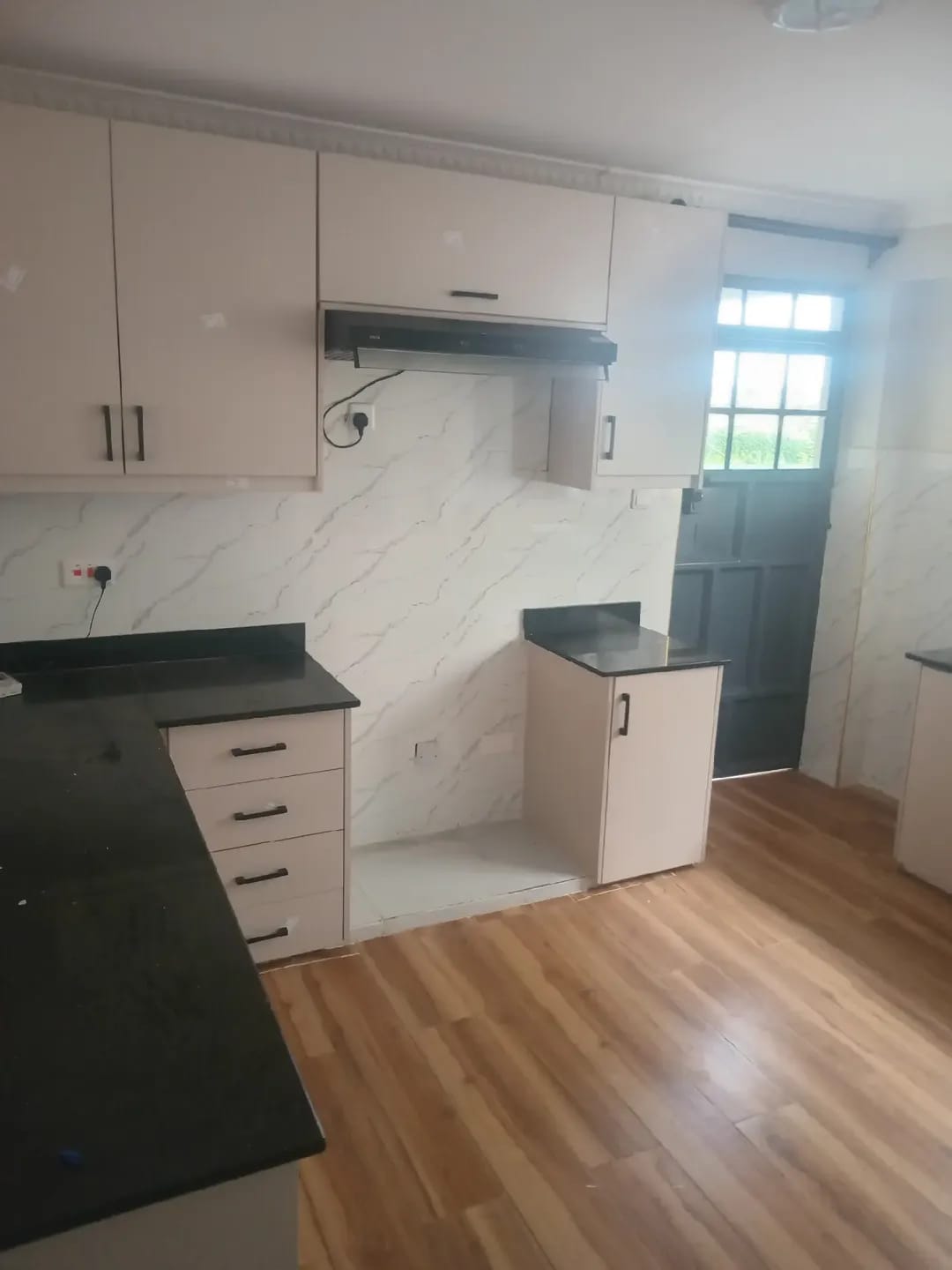 Kitchen in Karen, Kerarapon with cream cabinets, black countertops, an extractor hood and wood-look flooring.