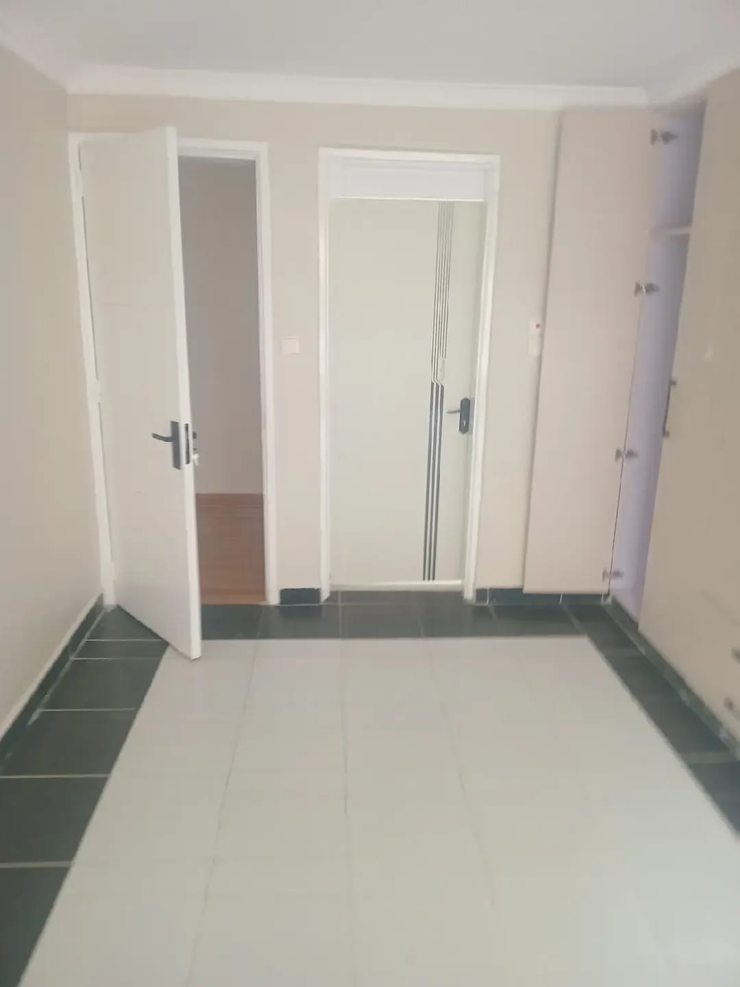 Unfurnished room in Karen, Kerarapon, with dark-bordered floor tiles, white doors and an open built-in cupboard.