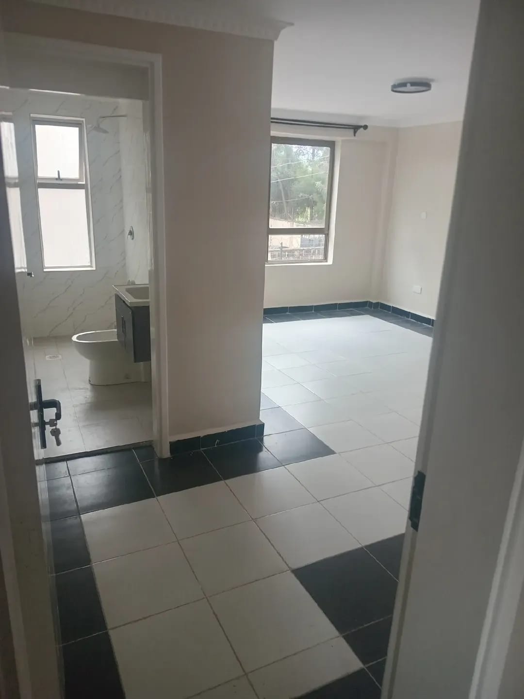 Unfurnished room with light floor tiles, dark borders and an adjoining bathroom in Karen, Kerarapon.