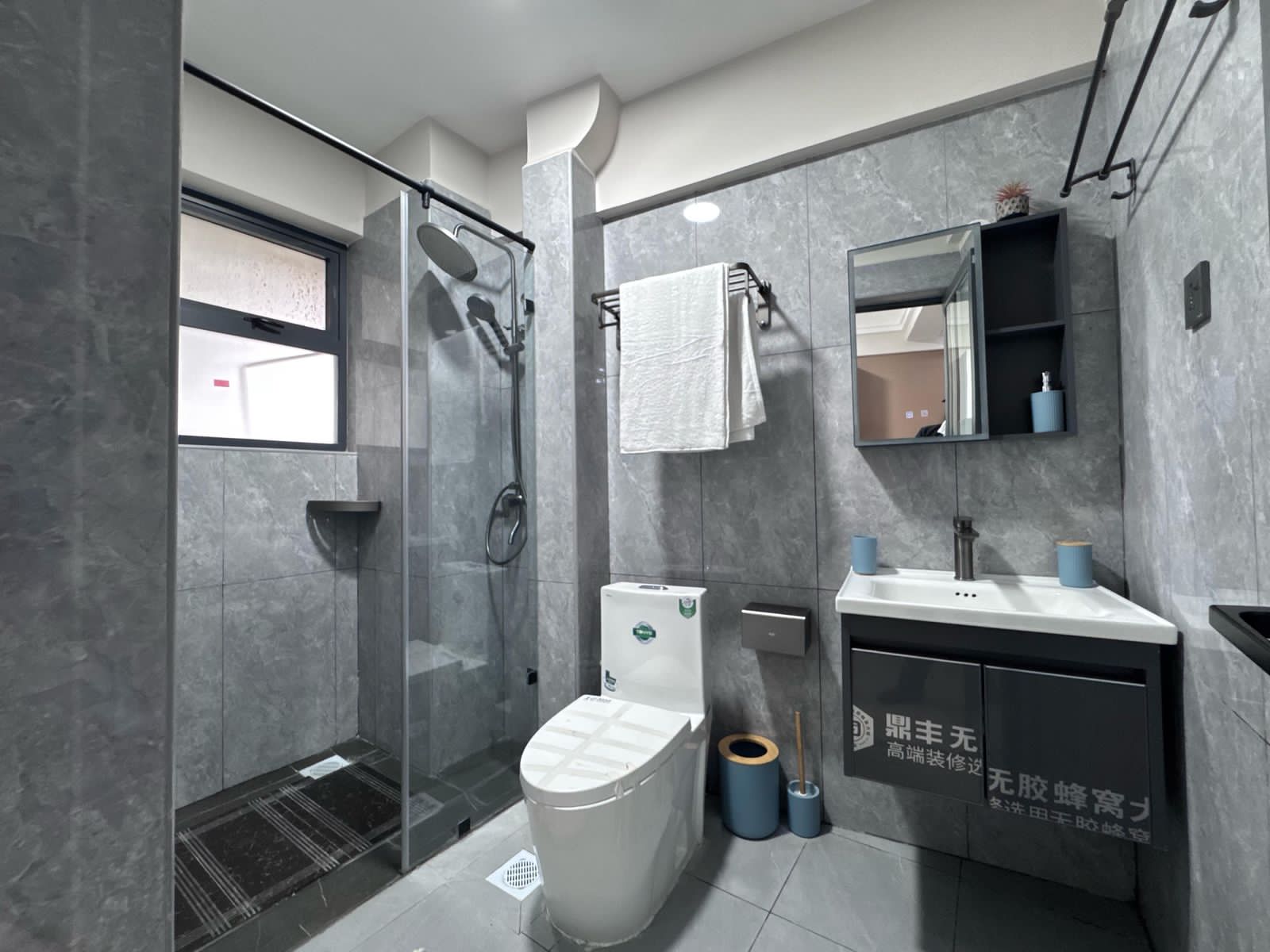 Kilimani apartment bathroom with grey tiles, glass shower screen, white toilet and wall-mounted vanity beneath a mirror.