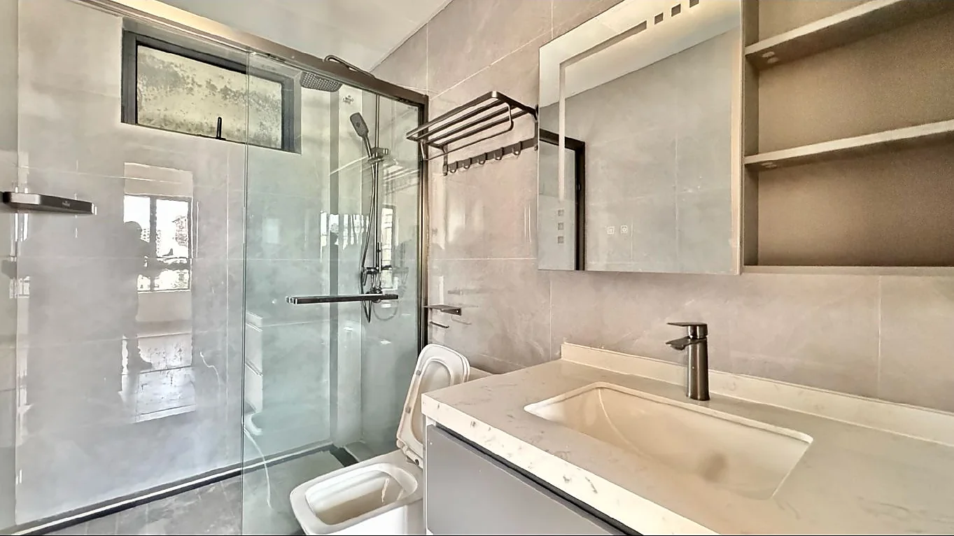 Bathroom in the Kilimani apartment with a glass-enclosed shower, toilet, vanity basin, mirror and open shelving.