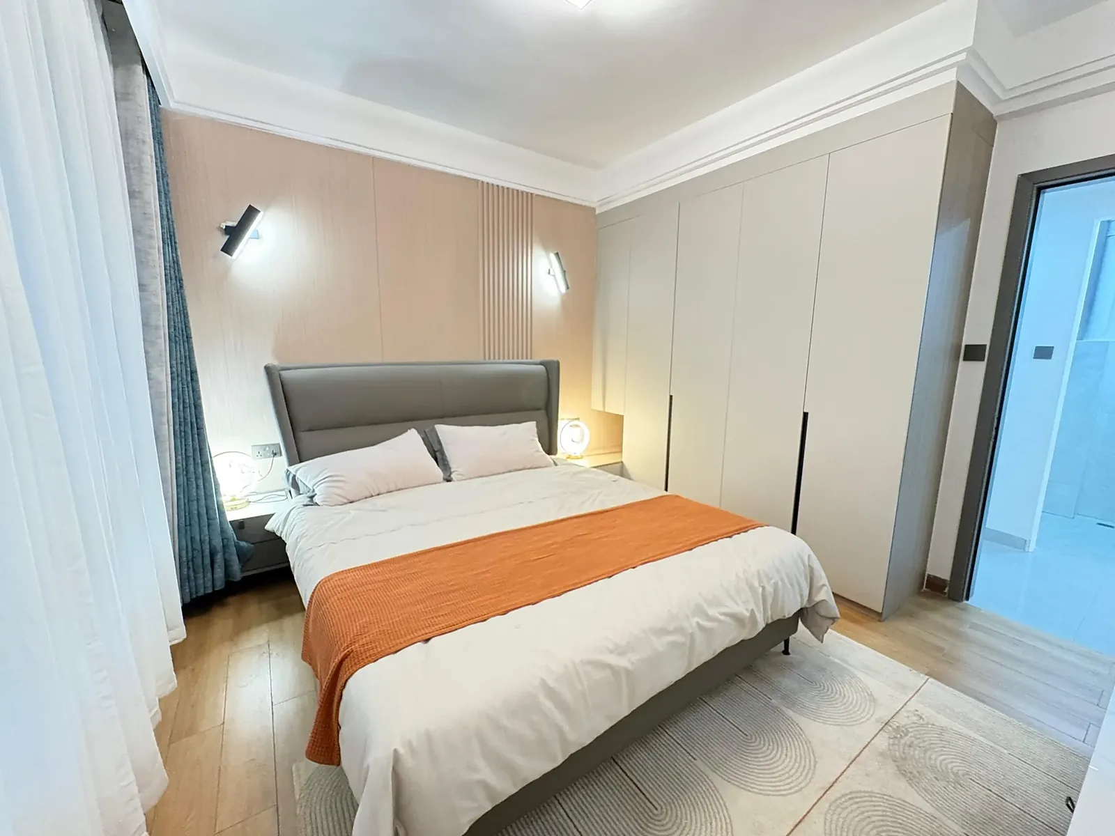 Bedroom in the Kilimani apartment with a grey upholstered bed, orange throw and full-height built-in wardrobes.