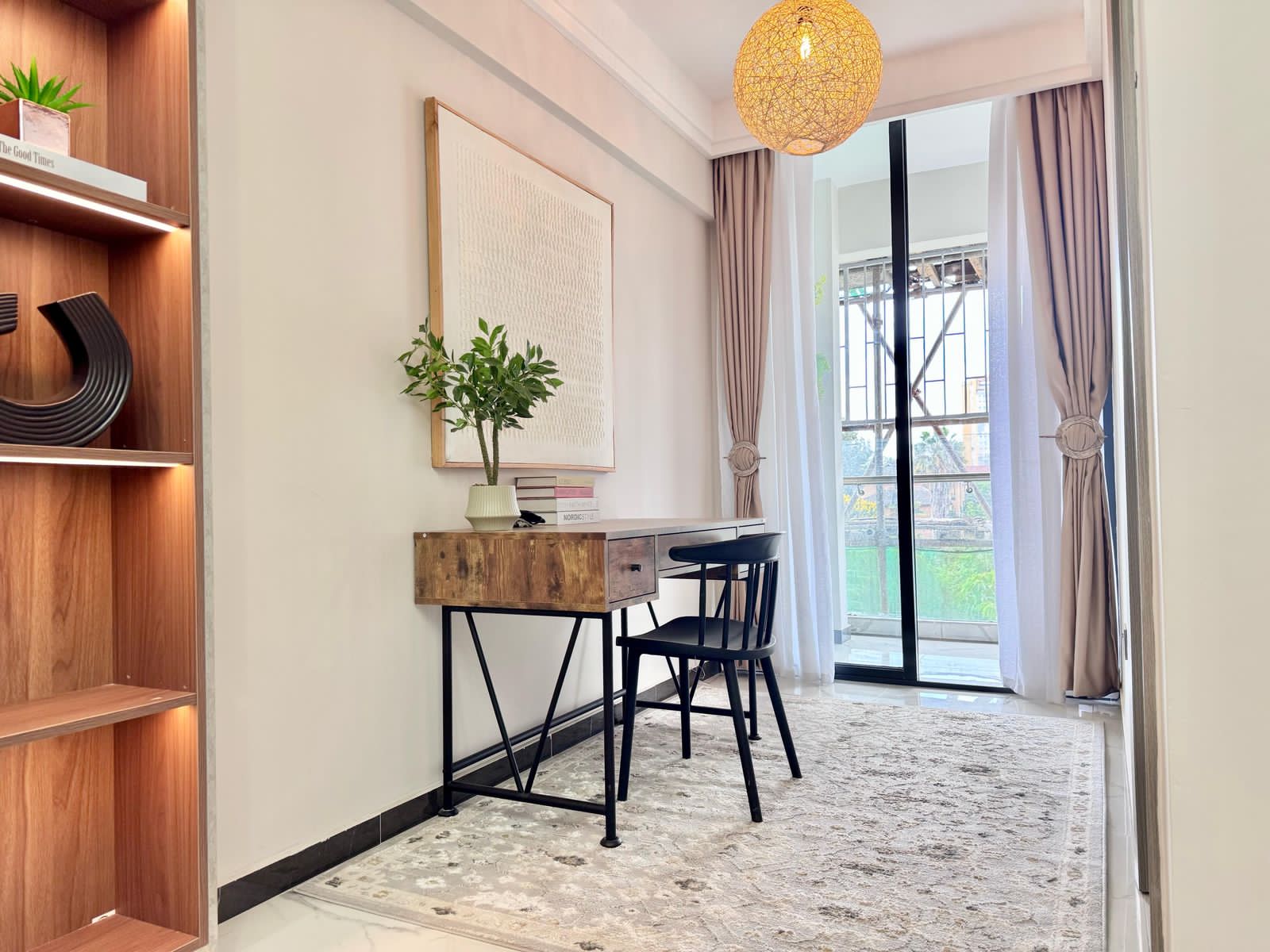 Wooden desk and black chair beside curtained sliding glass doors in the Kilimani apartment.