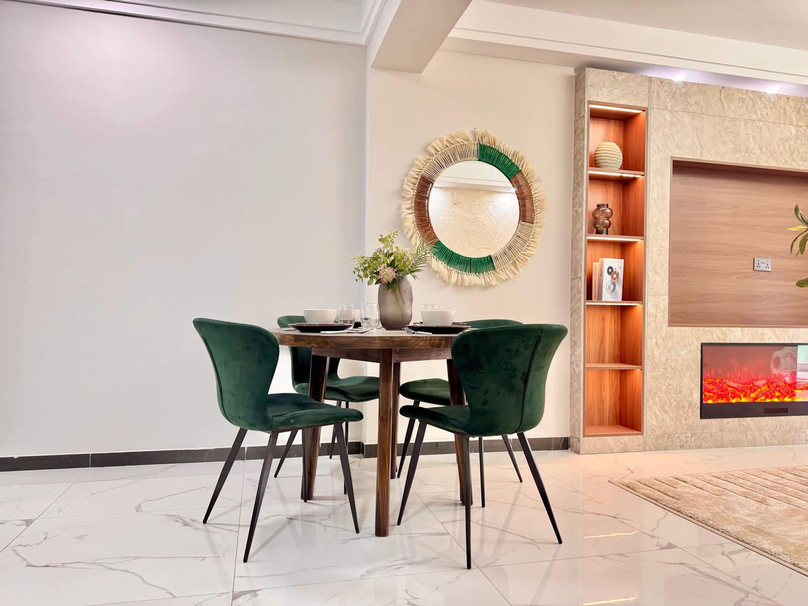 Kilimani apartment dining area with a wooden table, green chairs, round mirror and illuminated shelving.