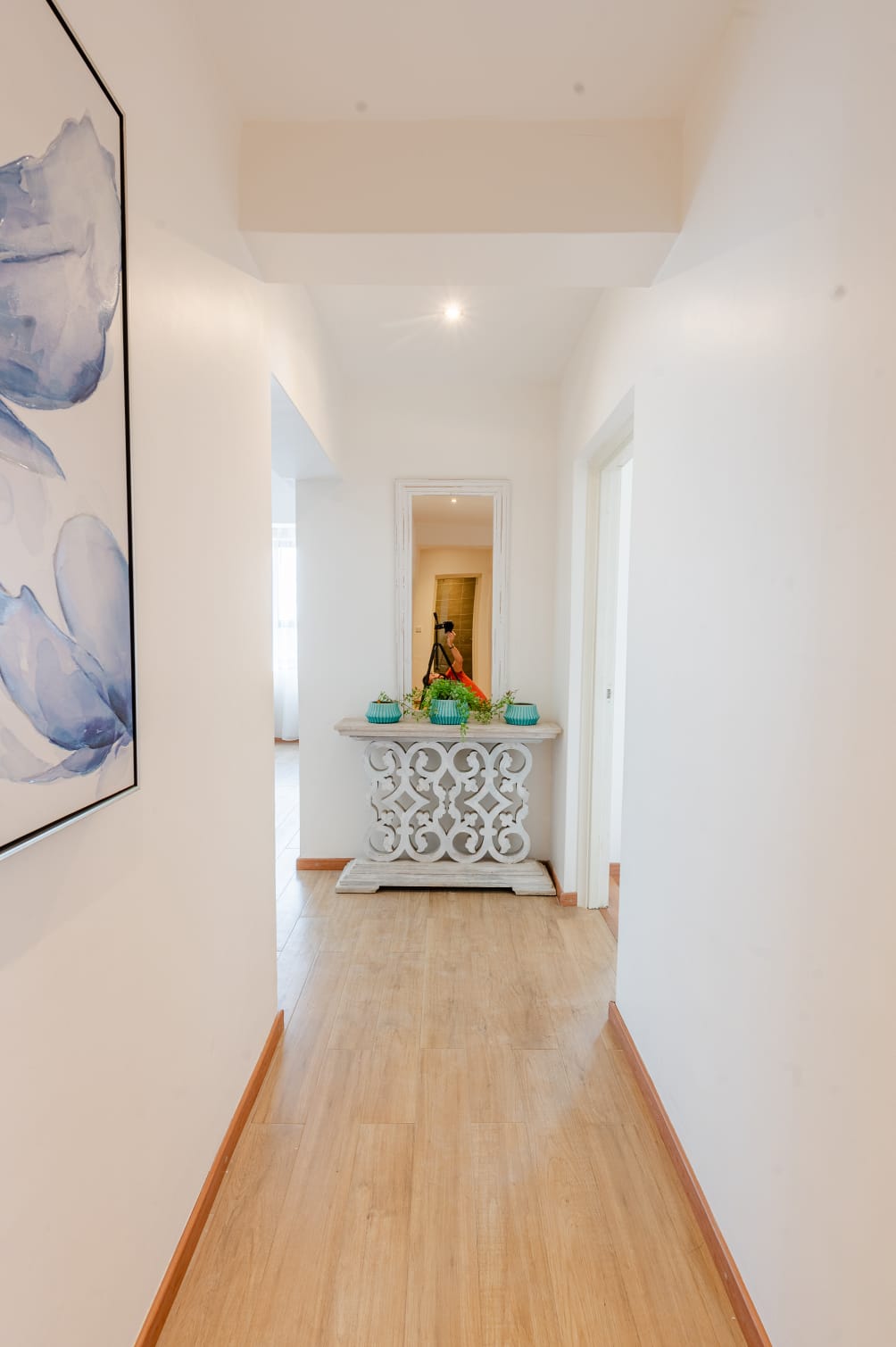 Kilimani apartment hallway with wood-look flooring, floral artwork, and an ornate console table beneath a wall mirror.