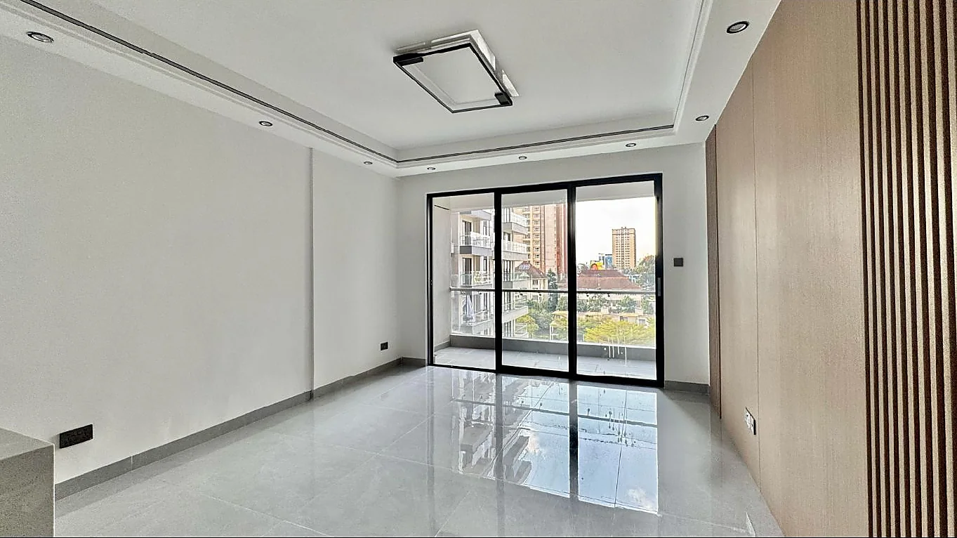 Unfurnished living area in Kilimani with glossy tiled flooring, a panelled accent wall and glass balcony doors.