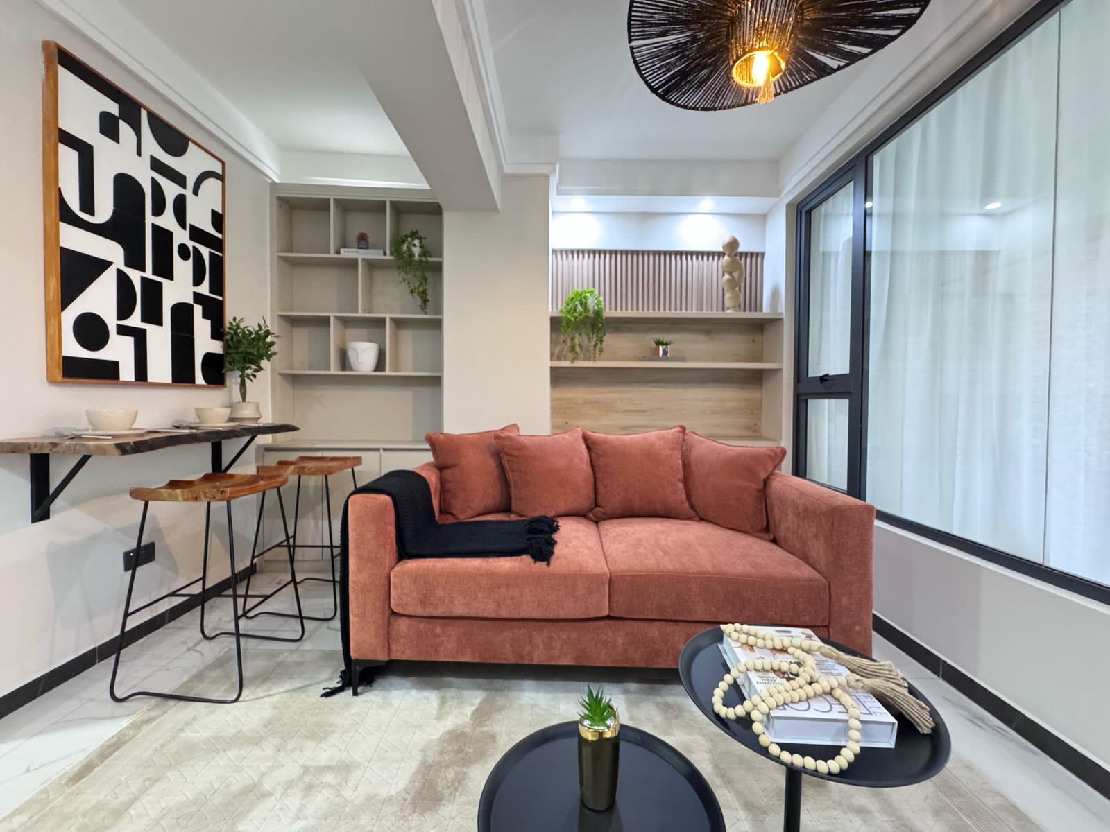 Kilimani apartment living area with a coral sofa, counter seating, open shelving and black coffee tables.