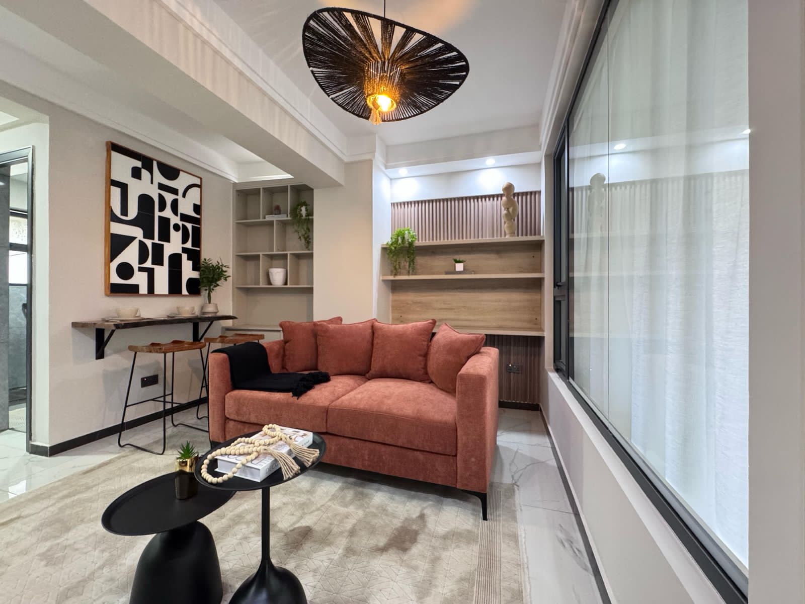 Kilimani apartment living area with a salmon sofa, black coffee tables, wall shelving and pendant light.