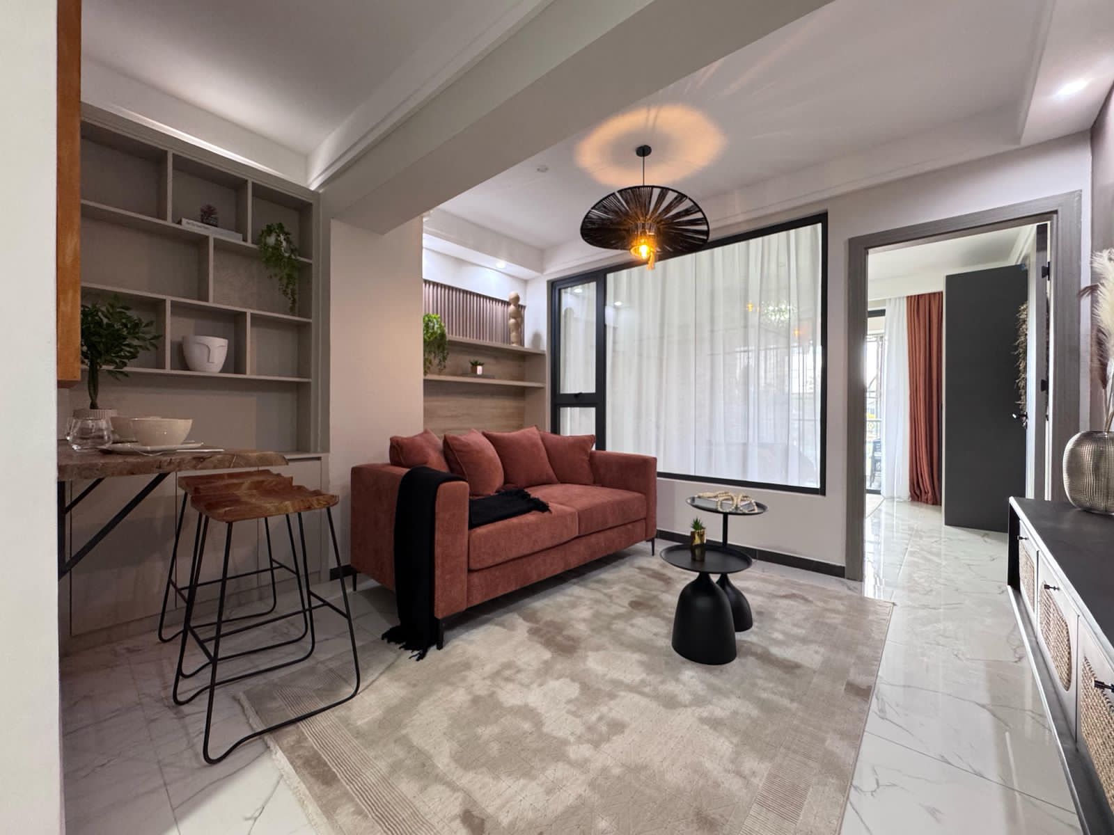Kilimani apartment living room with a rust-coloured sofa, black round tables, open shelving and bar stools.