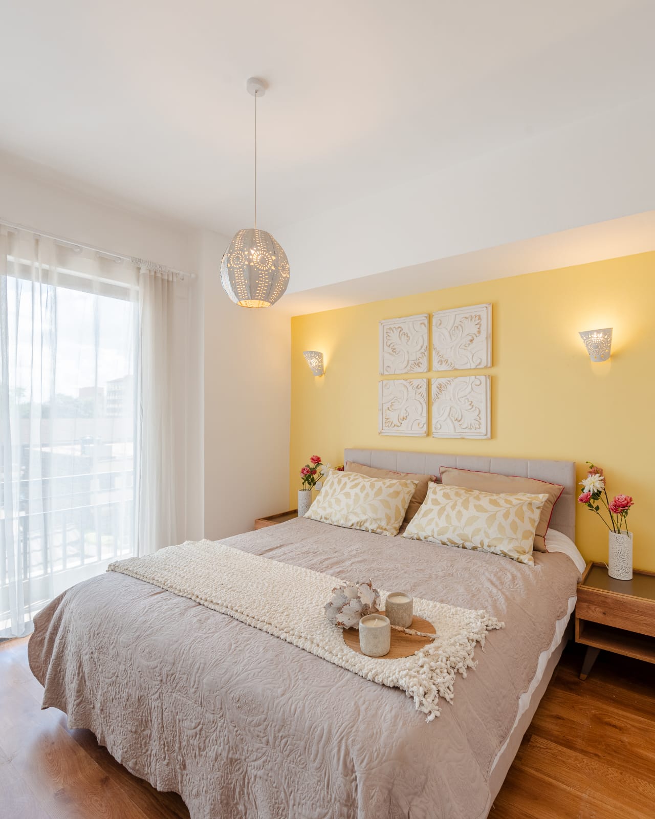 Furnished Kilimani bedroom with a yellow accent wall, double bed, pendant light and sheer white curtains.