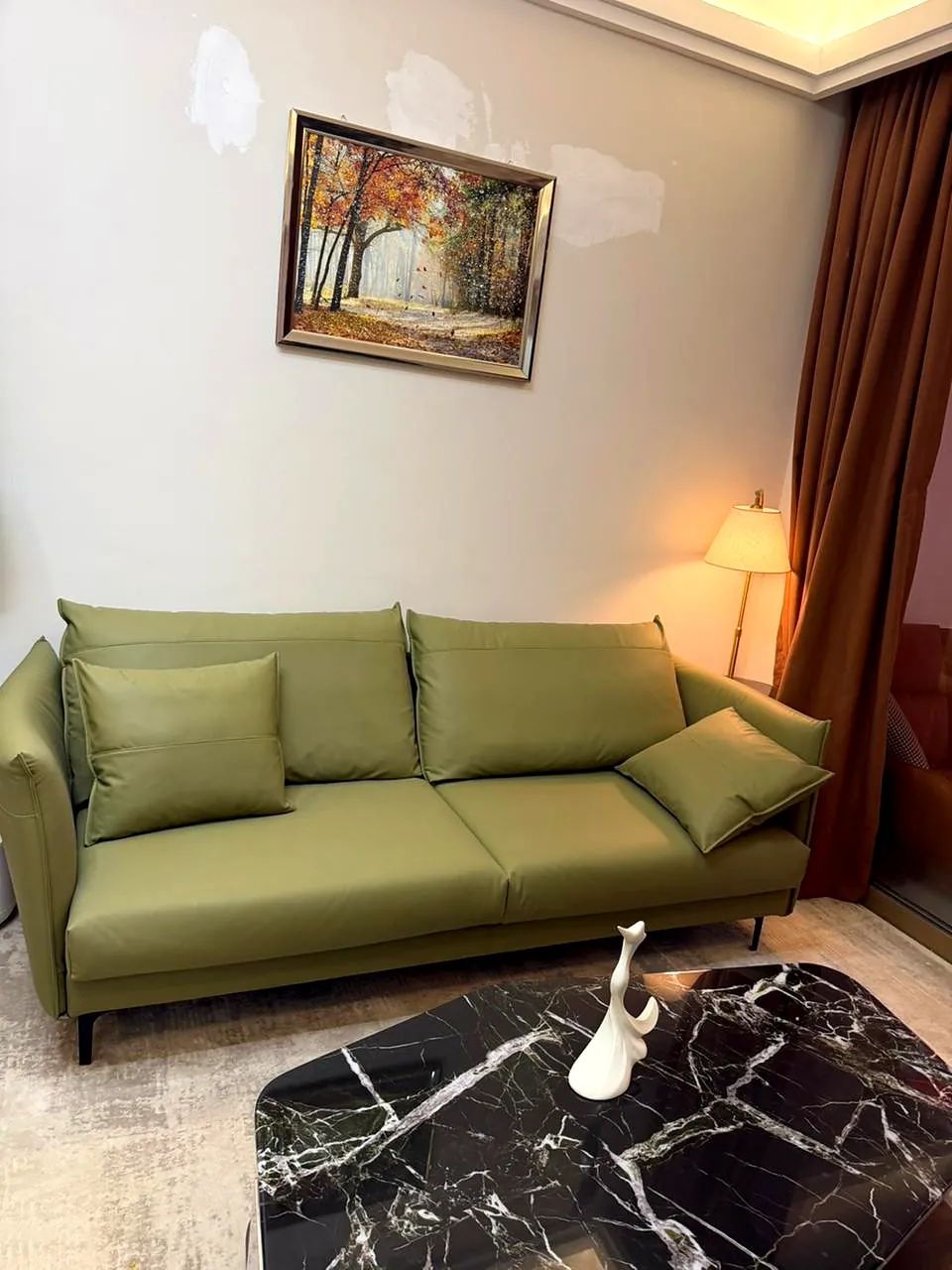 Green sofa, black coffee table and framed woodland artwork at Lido Garden Apartments in Kilimani.