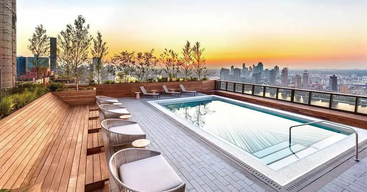 Rooftop pool at Lilydale Riverside with lounge chairs, trees and a city skyline at sunset.