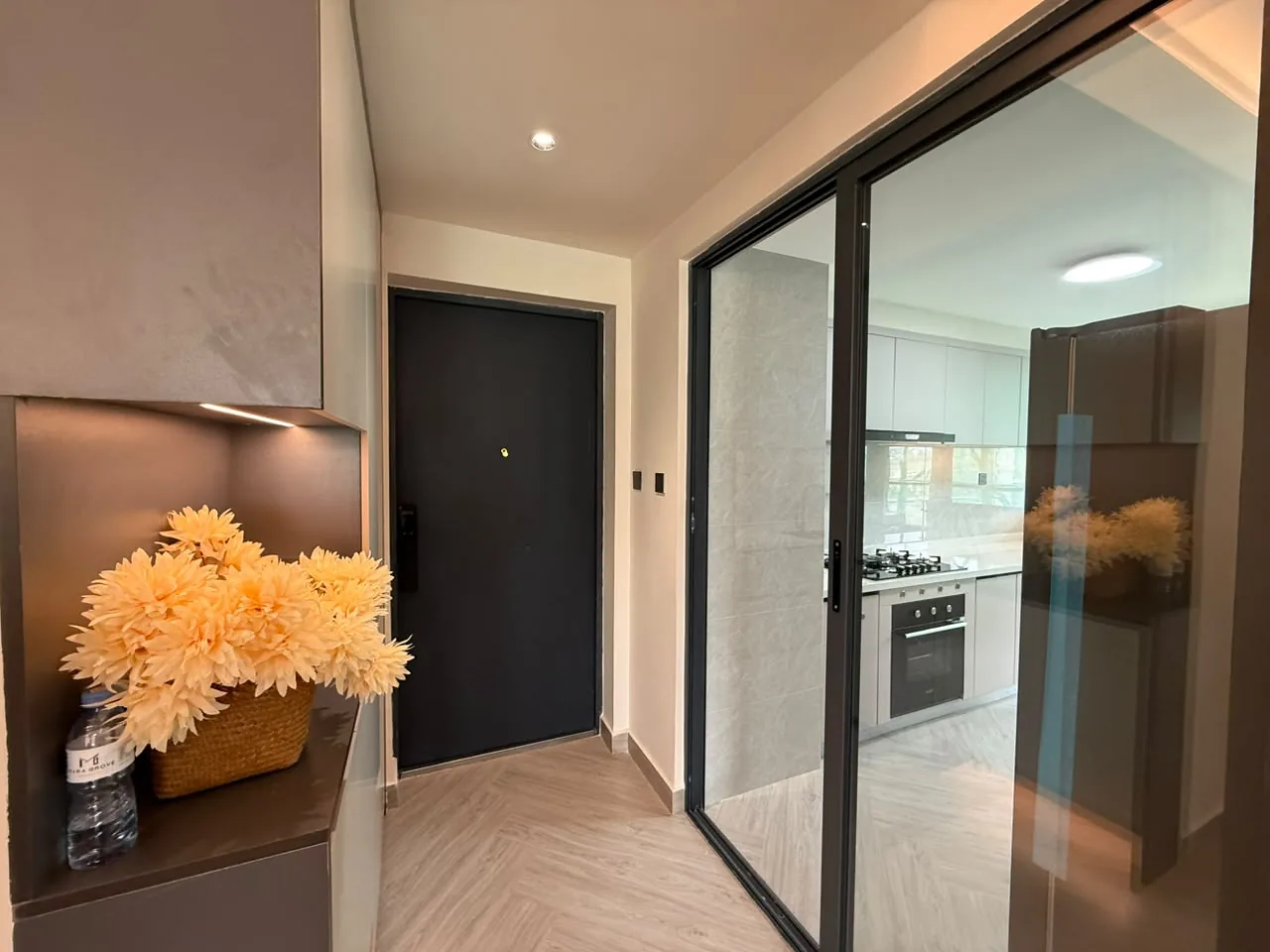 Entryway at Mara Grove Residence, Syokimau, with built-in storage and a glass sliding door to the kitchen.