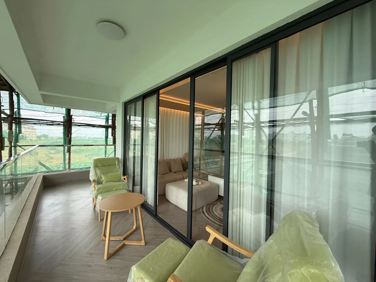 Balcony at Mara Grove Residence with green chairs, a small table, glass railing and sliding glass doors.