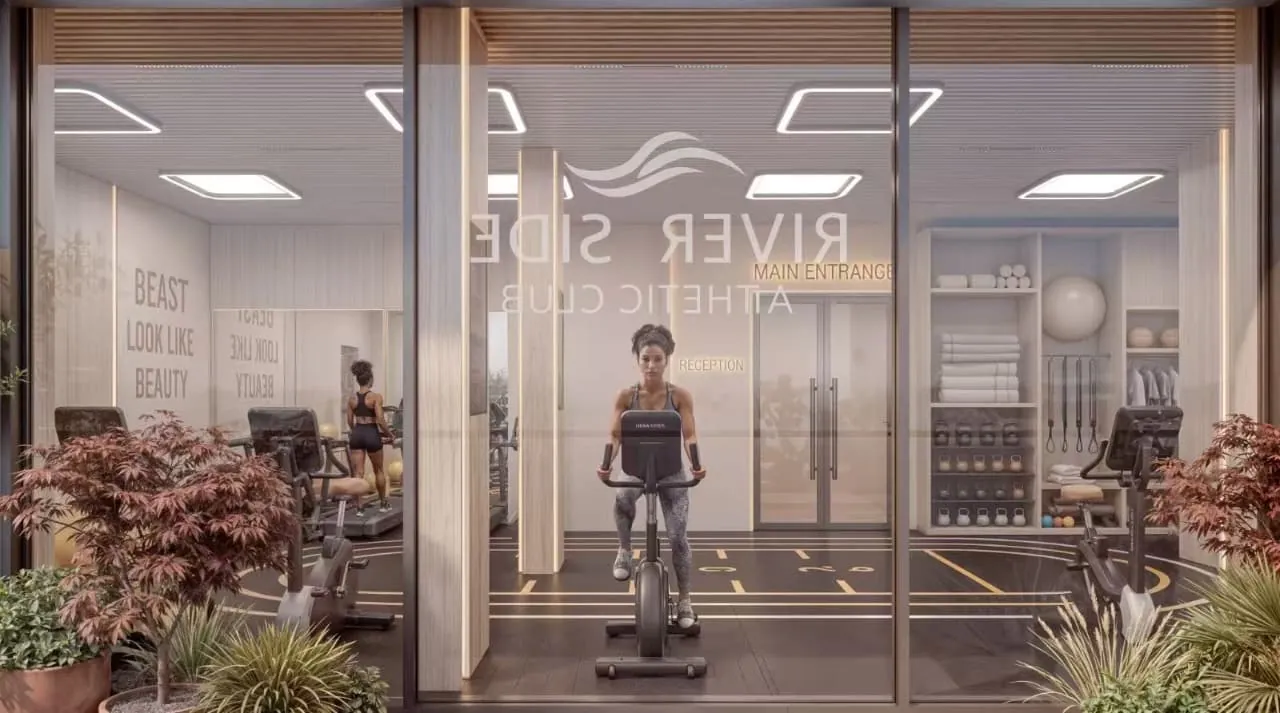 Gym rendering at Riverside Times Apartments, showing stationary bikes and weight storage behind floor-to-ceiling glass.