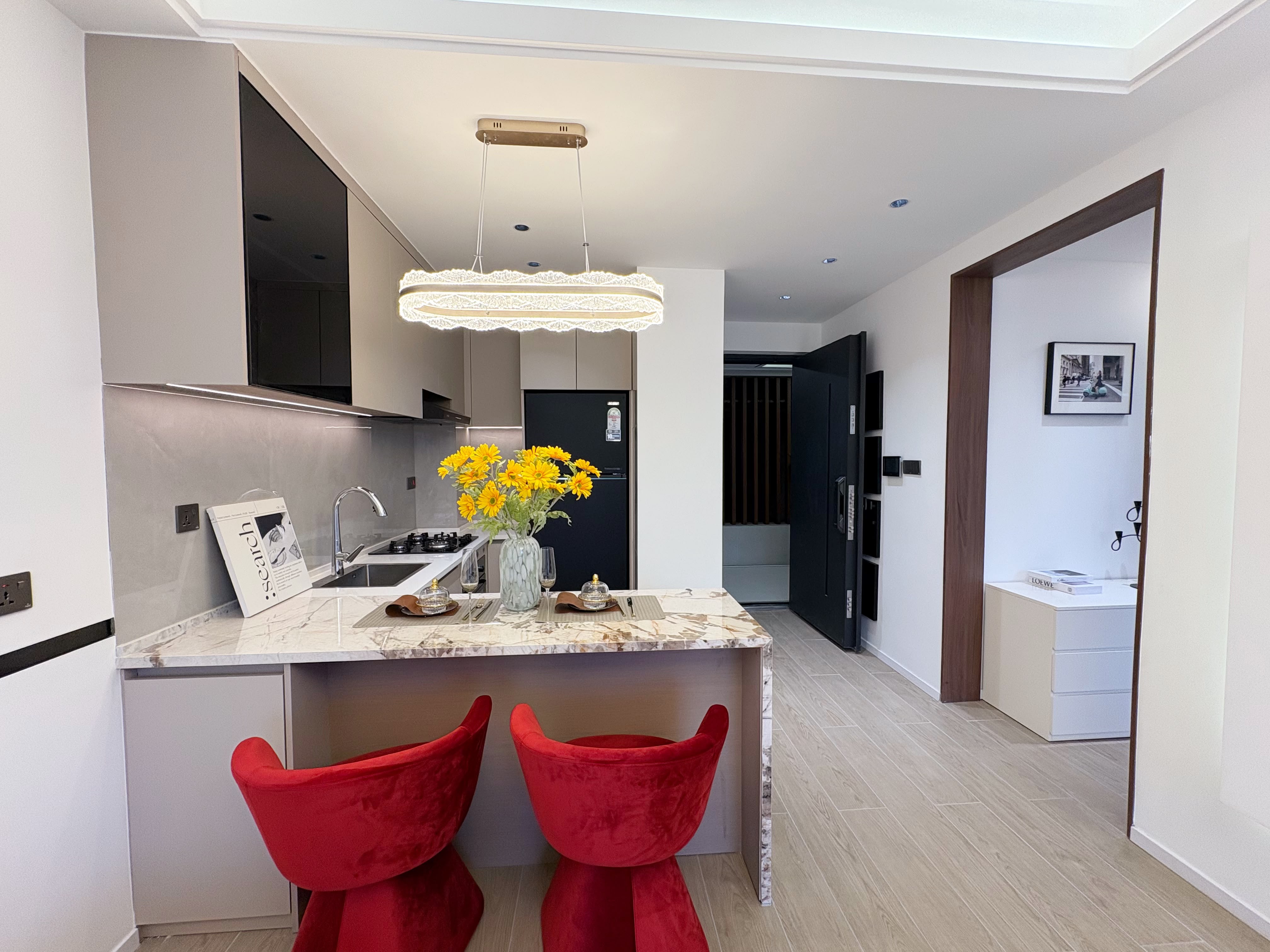Kitchen at Santorini Residences, Westlands, with a breakfast bar, two red chairs and pendant lighting.