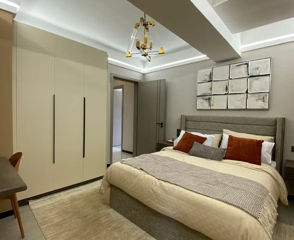 Bedroom at Super Westbury, Westlands, with an upholstered bed, cream wardrobes, abstract wall art and geometric pendant lighting.