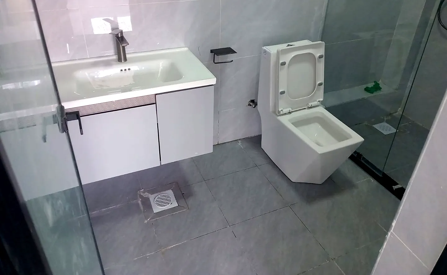 Grey-tiled bathroom at Versailles Garden, Kileleshwa, with a white vanity, toilet and glass shower enclosure.