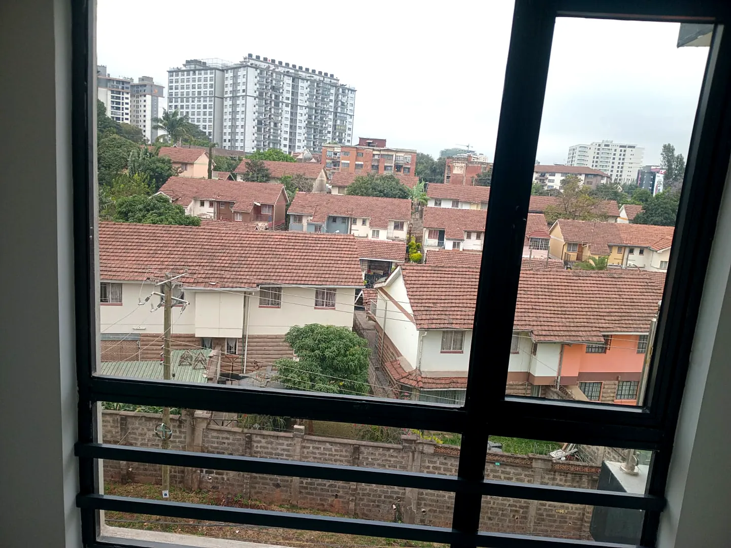 Window view from Versailles Garden, Kileleshwa, overlooking red-roofed houses, trees and high-rise apartment buildings.