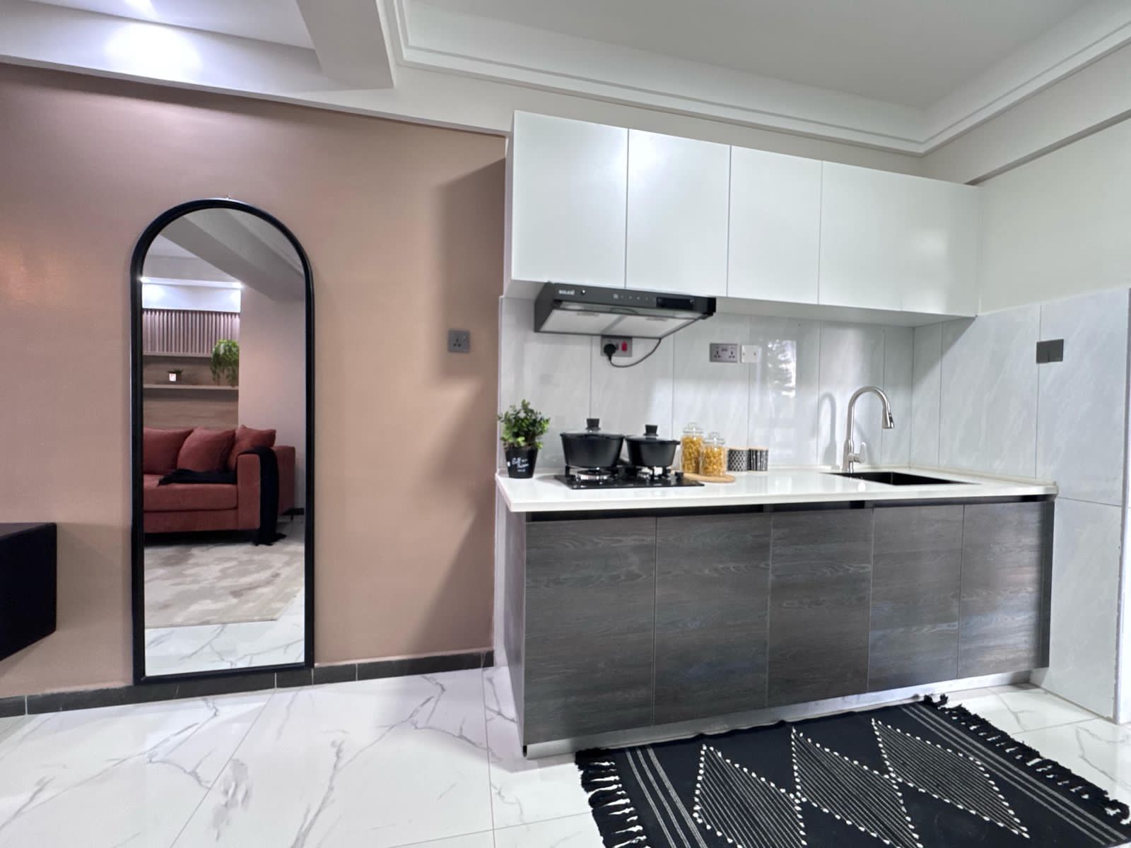 Kilimani apartment kitchen with white upper cabinets, grey lower cabinets, a hob, extractor hood and sink.